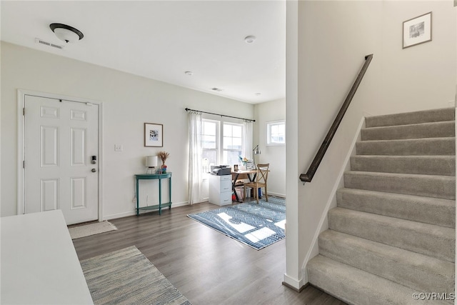 foyer entrance with visible vents, baseboards, wood finished floors, and stairway