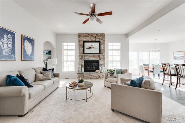 living room with a stone fireplace, ceiling fan with notable chandelier, a healthy amount of sunlight, and carpet floors