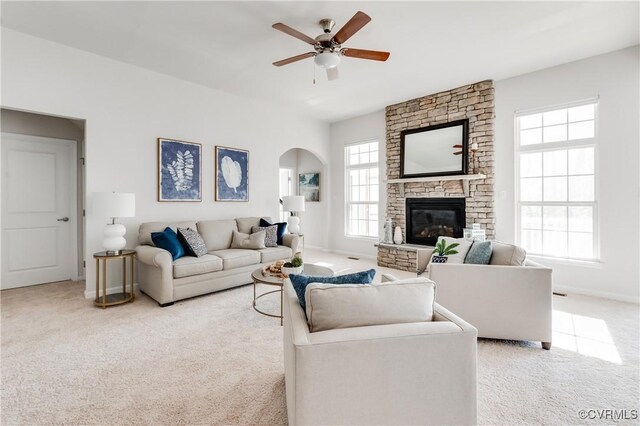 living room featuring baseboards, a fireplace, arched walkways, ceiling fan, and light carpet