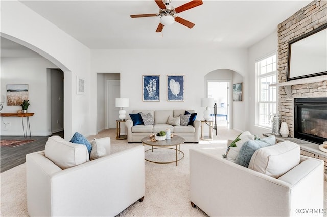 living room featuring visible vents, baseboards, a stone fireplace, arched walkways, and a ceiling fan