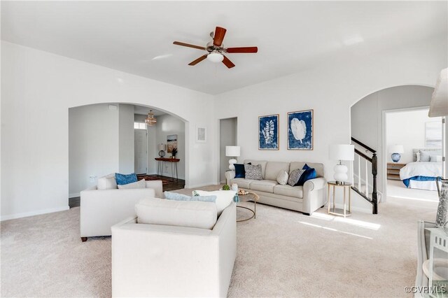 carpeted living area featuring arched walkways, baseboards, stairs, and a ceiling fan