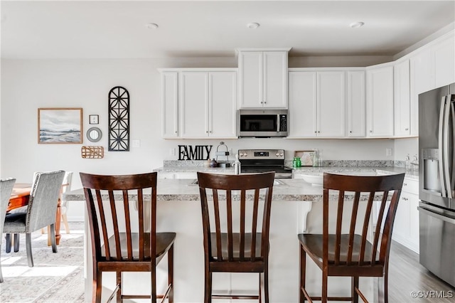 kitchen with white cabinetry, a kitchen breakfast bar, a center island with sink, and stainless steel appliances