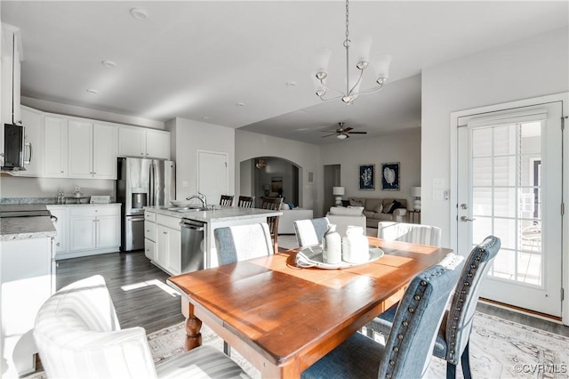 dining area with wood finished floors, ceiling fan with notable chandelier, and arched walkways