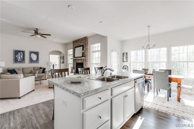 kitchen featuring a sink, a stone fireplace, light countertops, dishwasher, and open floor plan