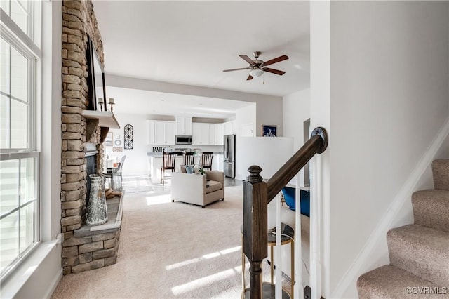 stairway featuring a healthy amount of sunlight, a fireplace, a ceiling fan, and carpet