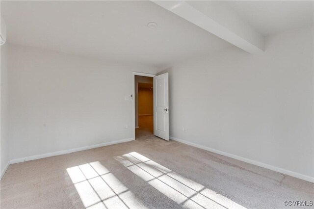 spare room featuring baseboards, light carpet, and beamed ceiling