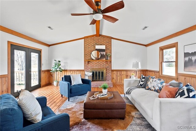 living area featuring wood finished floors, vaulted ceiling with beams, a fireplace, and wainscoting