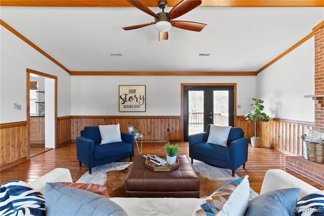 living area with visible vents, wood-type flooring, ornamental molding, and wainscoting