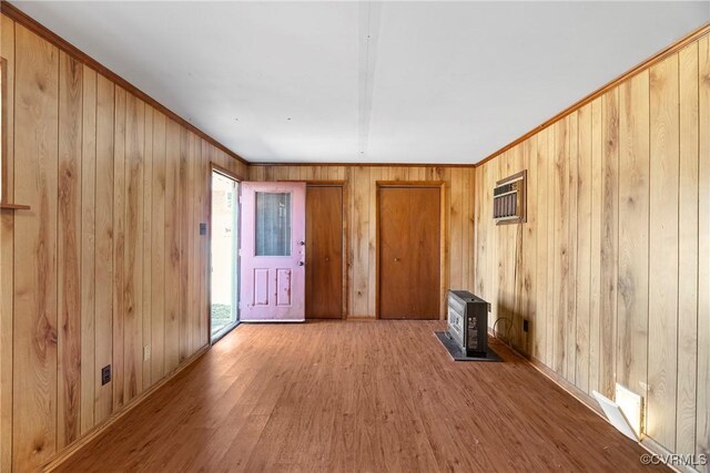 spare room with wooden walls, ornamental molding, a wood stove, and wood finished floors