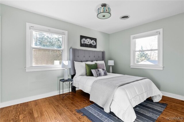 bedroom featuring multiple windows, wood finished floors, visible vents, and baseboards