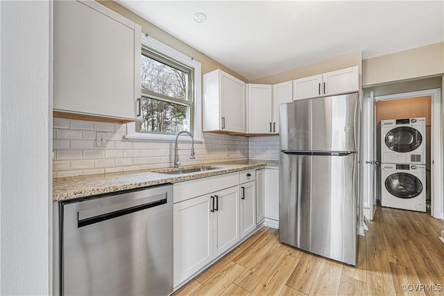 kitchen with light wood-style flooring, a sink, stacked washing maching and dryer, appliances with stainless steel finishes, and light stone countertops