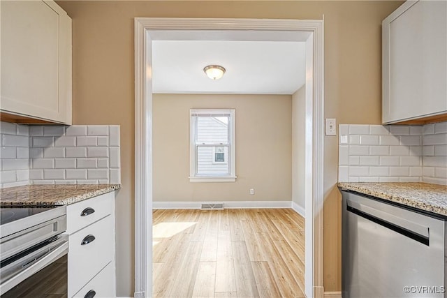 kitchen featuring light stone counters, visible vents, baseboards, light wood-style floors, and tasteful backsplash