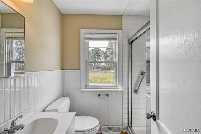 full bath featuring a healthy amount of sunlight, toilet, tiled shower, and wainscoting