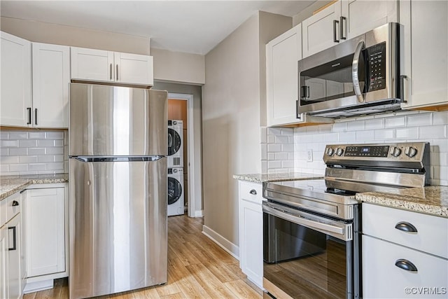 kitchen with stainless steel appliances, light wood-style flooring, stacked washer / drying machine, and white cabinetry