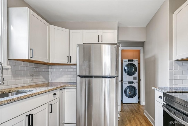 kitchen featuring a sink, white cabinetry, stacked washer and clothes dryer, and freestanding refrigerator