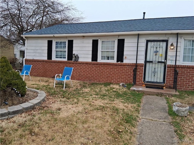 view of front of property featuring brick siding and roof with shingles