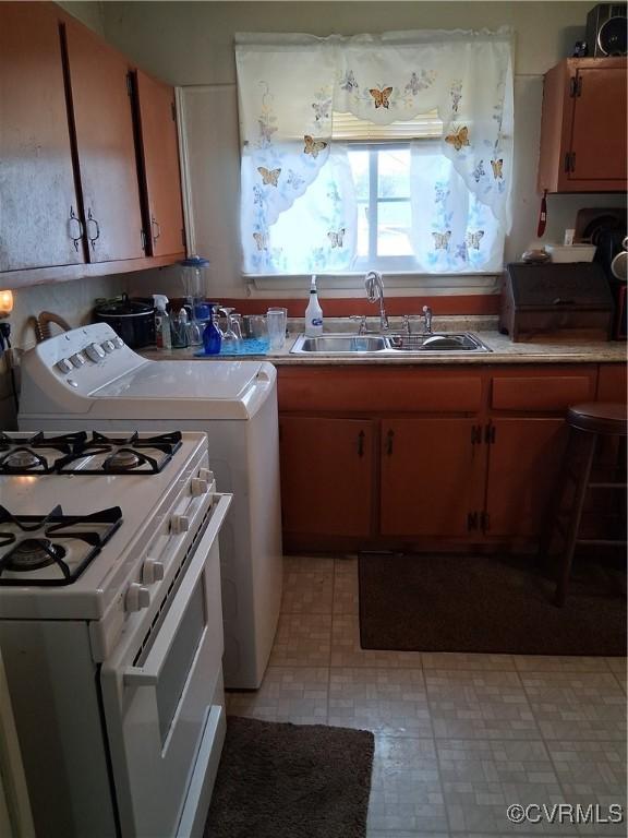 kitchen with white range with gas cooktop, light floors, light countertops, and a sink