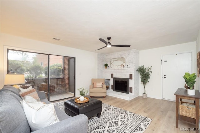 living room featuring visible vents, a brick fireplace, light wood-type flooring, and ceiling fan