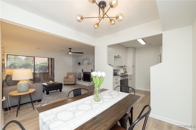 dining area with a large fireplace, ceiling fan with notable chandelier, light wood-type flooring, and baseboards