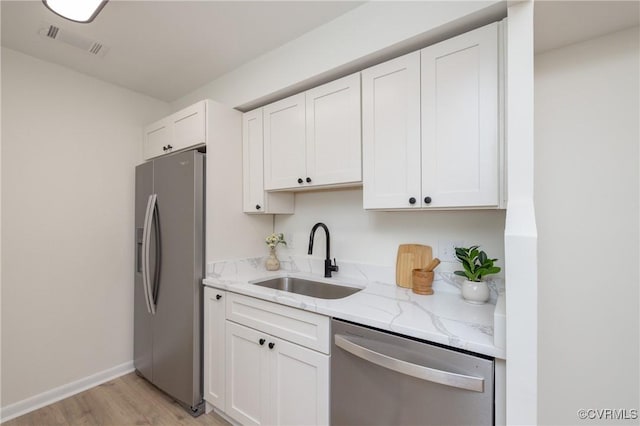 kitchen featuring visible vents, a sink, stainless steel appliances, white cabinets, and light stone countertops