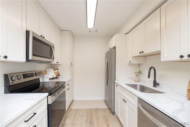 kitchen with light stone countertops, light wood-type flooring, appliances with stainless steel finishes, white cabinetry, and a sink