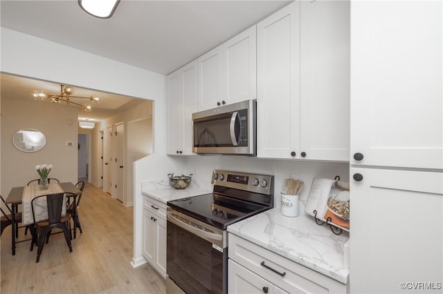 kitchen featuring light stone counters, stainless steel appliances, white cabinets, light wood-style floors, and a notable chandelier