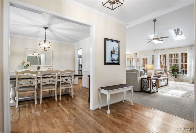 dining space featuring vaulted ceiling with skylight, wood finished floors, crown molding, and ceiling fan with notable chandelier