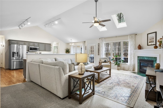 living room with ceiling fan, light wood-type flooring, a premium fireplace, a skylight, and high vaulted ceiling