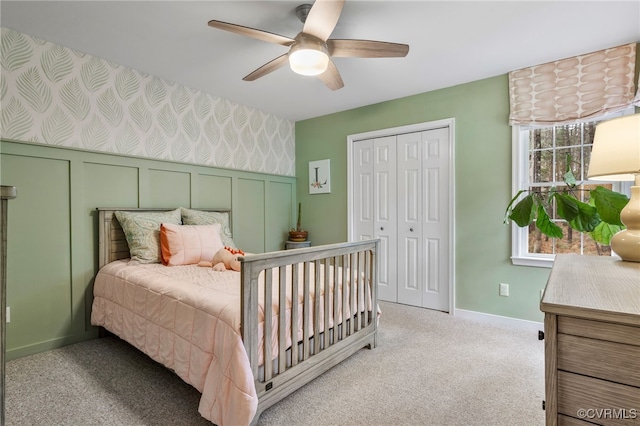 bedroom with wallpapered walls, a wainscoted wall, light colored carpet, a closet, and a ceiling fan