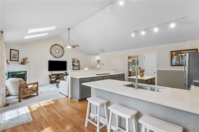 kitchen featuring gray cabinetry, light wood-style flooring, vaulted ceiling with skylight, freestanding refrigerator, and a sink