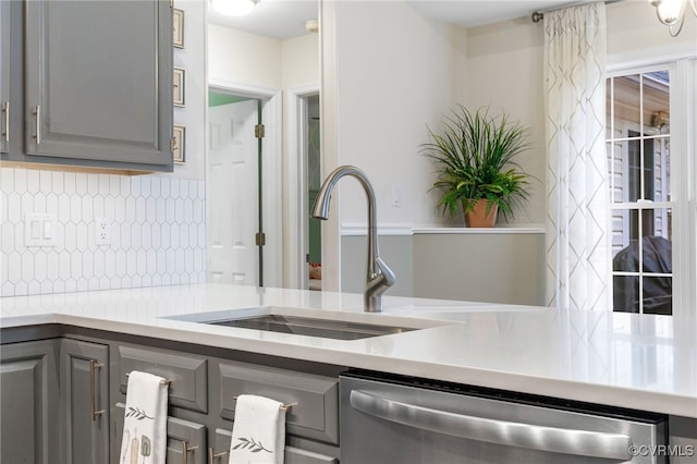 kitchen featuring stainless steel dishwasher, a sink, tasteful backsplash, and gray cabinetry