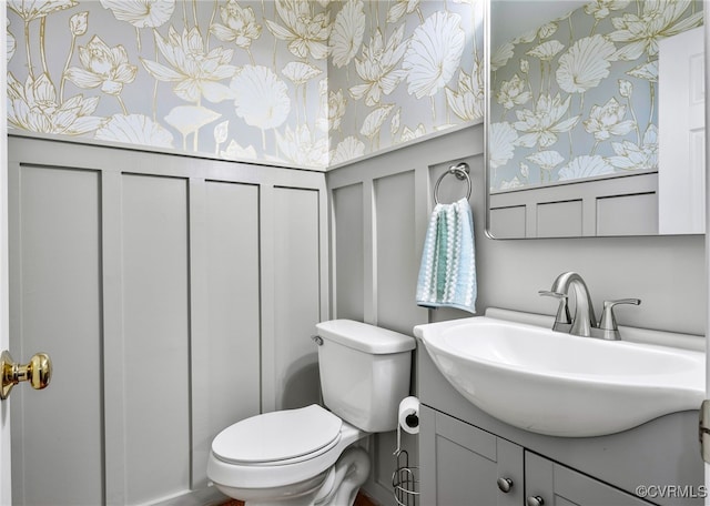 bathroom with a decorative wall, wallpapered walls, toilet, and vanity