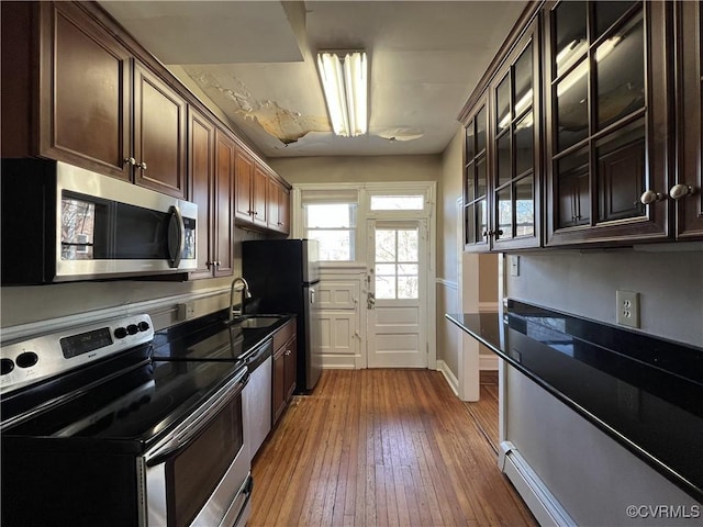 kitchen with hardwood / wood-style floors, a sink, stainless steel appliances, dark brown cabinetry, and glass insert cabinets