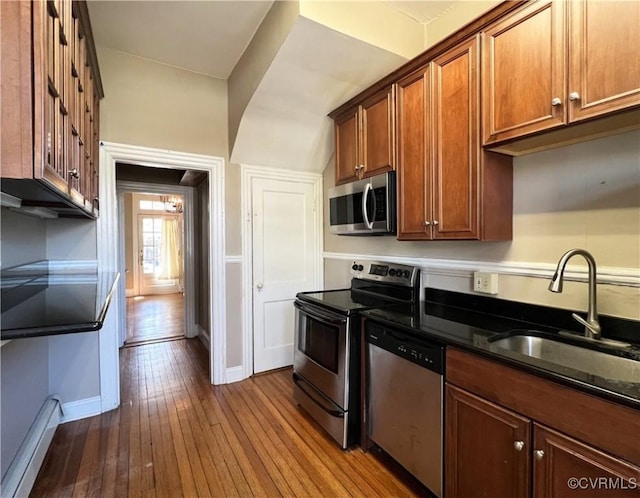 kitchen with brown cabinetry, baseboards, a sink, dark wood-type flooring, and appliances with stainless steel finishes