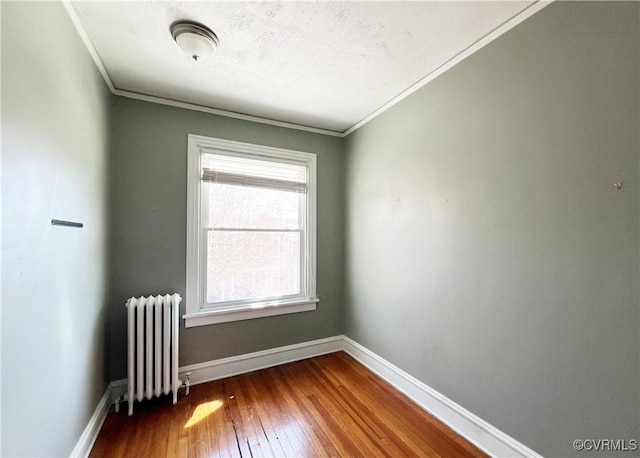 unfurnished room with ornamental molding, radiator heating unit, baseboards, and hardwood / wood-style flooring