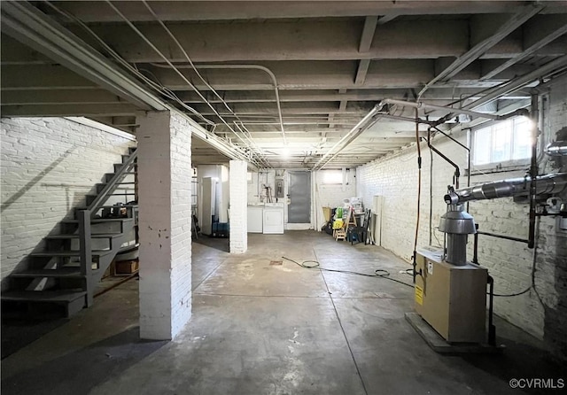 basement featuring stairway, washing machine and dryer, and brick wall