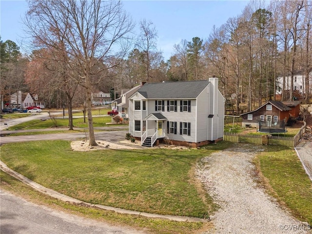 view of front of house featuring a front lawn, a chimney, driveway, and fence