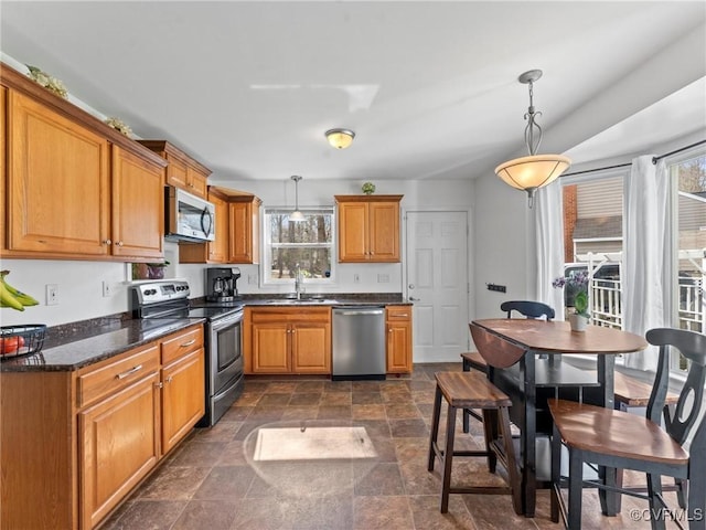 kitchen featuring brown cabinetry, stainless steel appliances, stone finish flooring, and decorative light fixtures