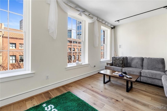 living area with a baseboard heating unit, a view of city, baseboards, and wood finished floors