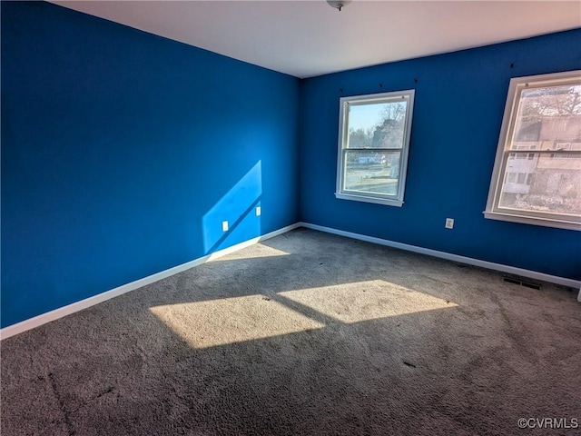 carpeted spare room with visible vents, a healthy amount of sunlight, and baseboards