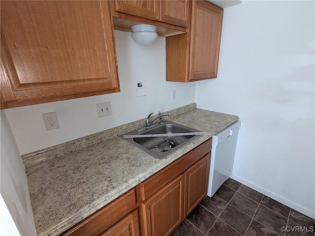 kitchen featuring dark tile patterned floors, a sink, brown cabinetry, baseboards, and dishwasher