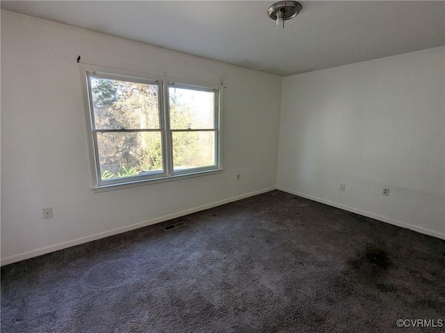 spare room featuring visible vents, baseboards, and dark colored carpet