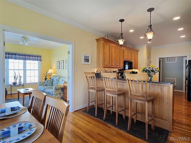 kitchen with ornamental molding, a peninsula, wood finished floors, hanging light fixtures, and black appliances