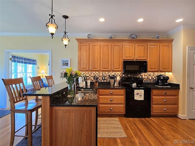 kitchen with tasteful backsplash, crown molding, a breakfast bar, light wood-style flooring, and black appliances