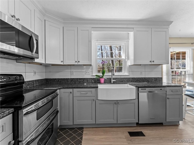 kitchen featuring a sink, dark stone countertops, light wood finished floors, and stainless steel appliances