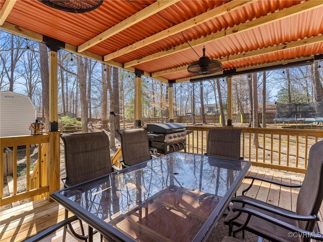 wooden deck with outdoor dining space, a trampoline, a ceiling fan, and a grill