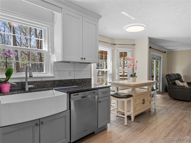 kitchen with dark stone countertops, light wood finished floors, a sink, a textured ceiling, and dishwasher