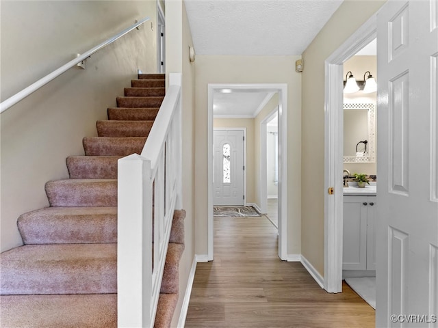 staircase featuring baseboards, a textured ceiling, wood finished floors, and ornamental molding