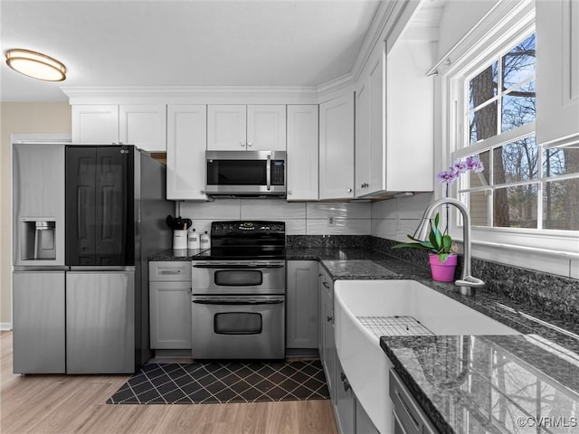 kitchen with dark stone counters, decorative backsplash, light wood-style floors, appliances with stainless steel finishes, and white cabinetry