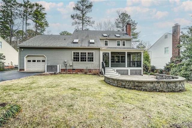 back of house featuring aphalt driveway, central air condition unit, a yard, a sunroom, and an attached garage